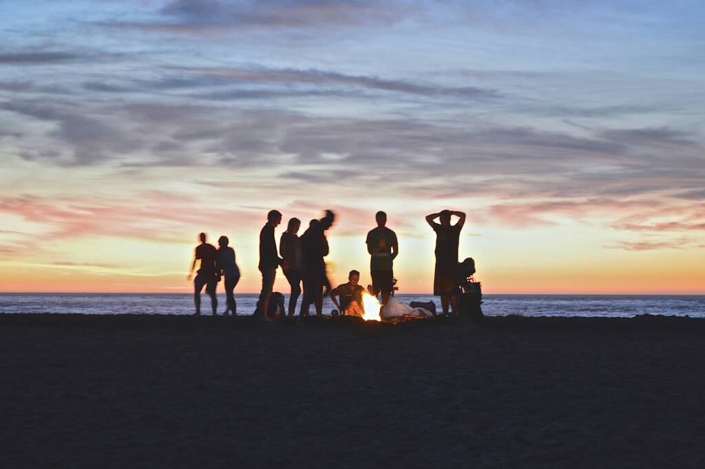Group silhouetted around a beach bonfire at sunset