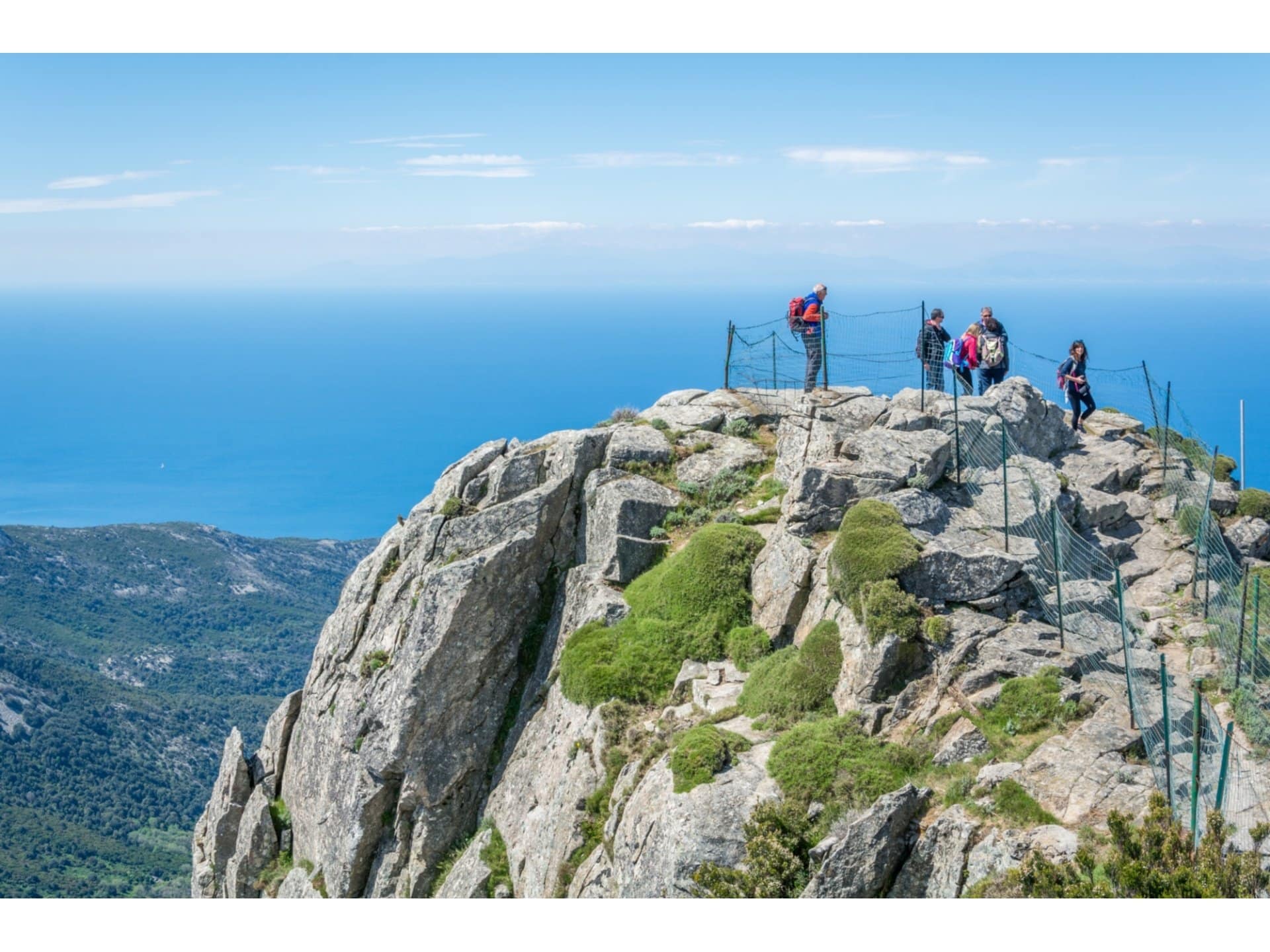 Hikers on a rocky summit above green hills and the sea in Tuscany