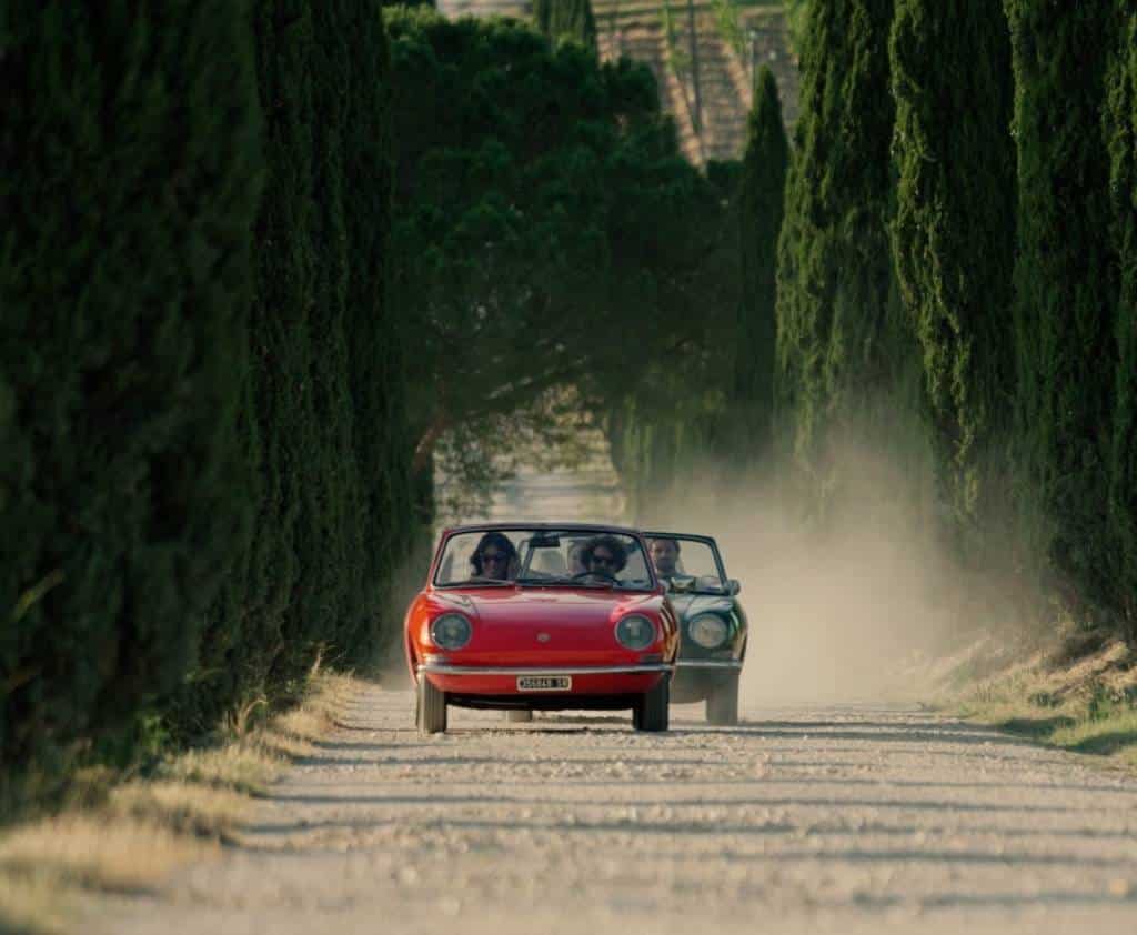 Vintage convertibles driving a cypress-lined gravel road in the Val d’Orcia