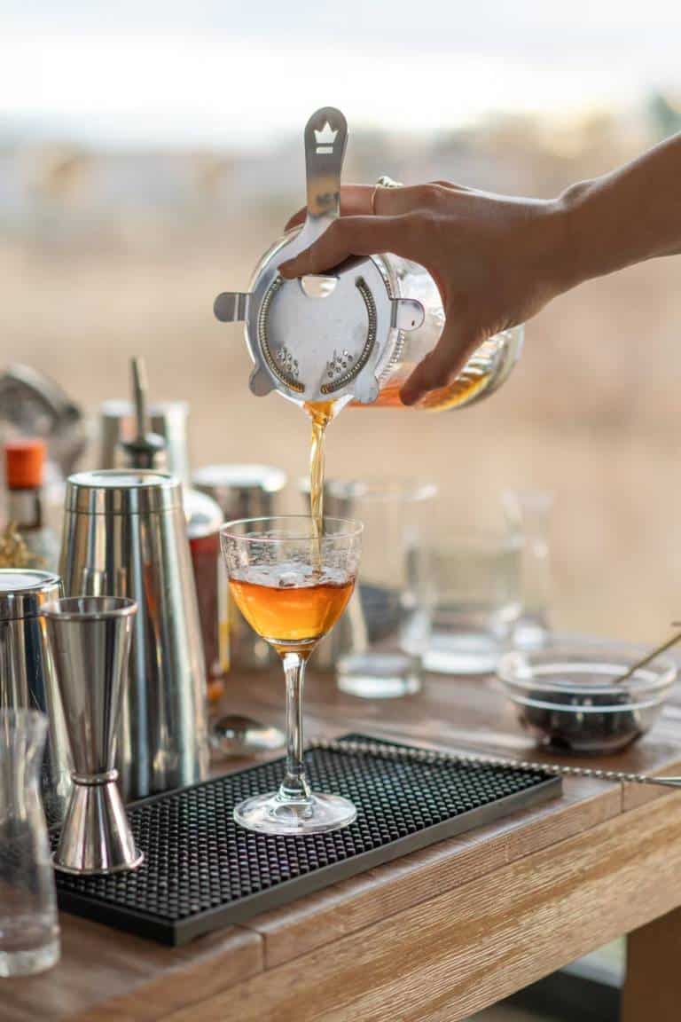 Bartender straining a botanical cocktail into a coupe