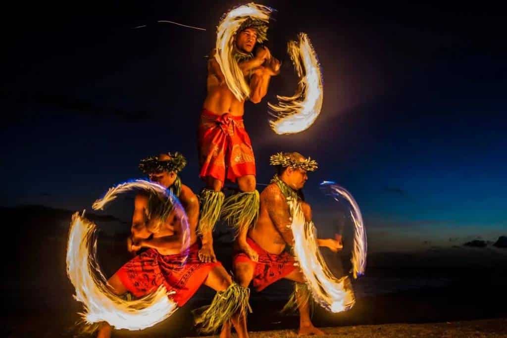 Fire knife dancers performing at a lūʻau at dusk
