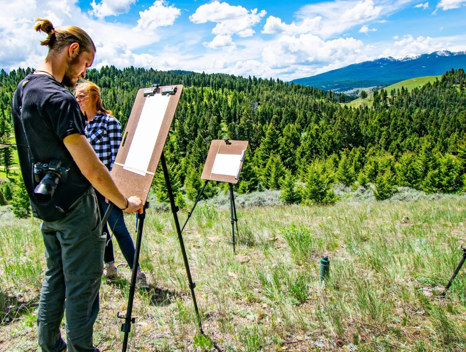 Two people painting at easels on a mountain hillside