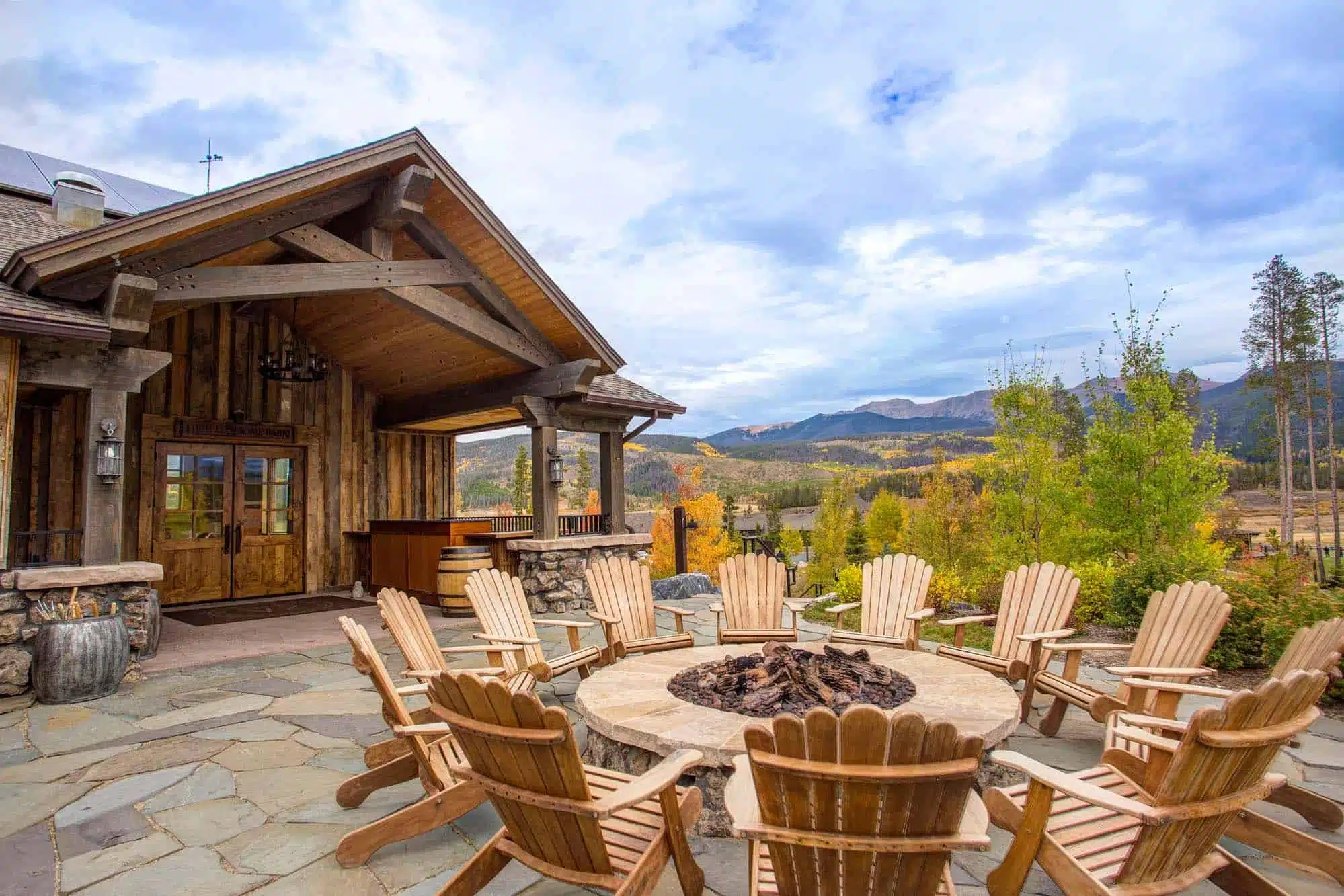 A circle of chairs around a fire pit outside a mountain lodge