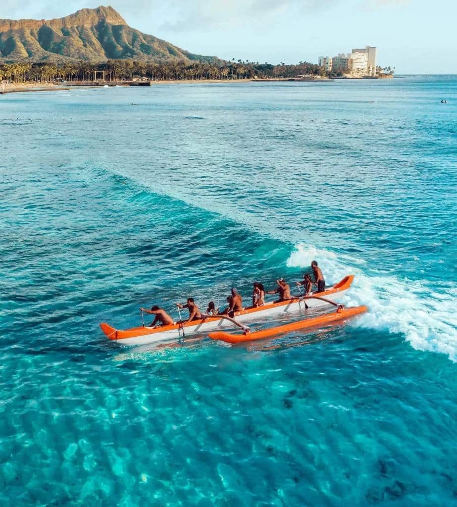 An outrigger canoe catching a wave off Waikīkī with Diamond Head behind