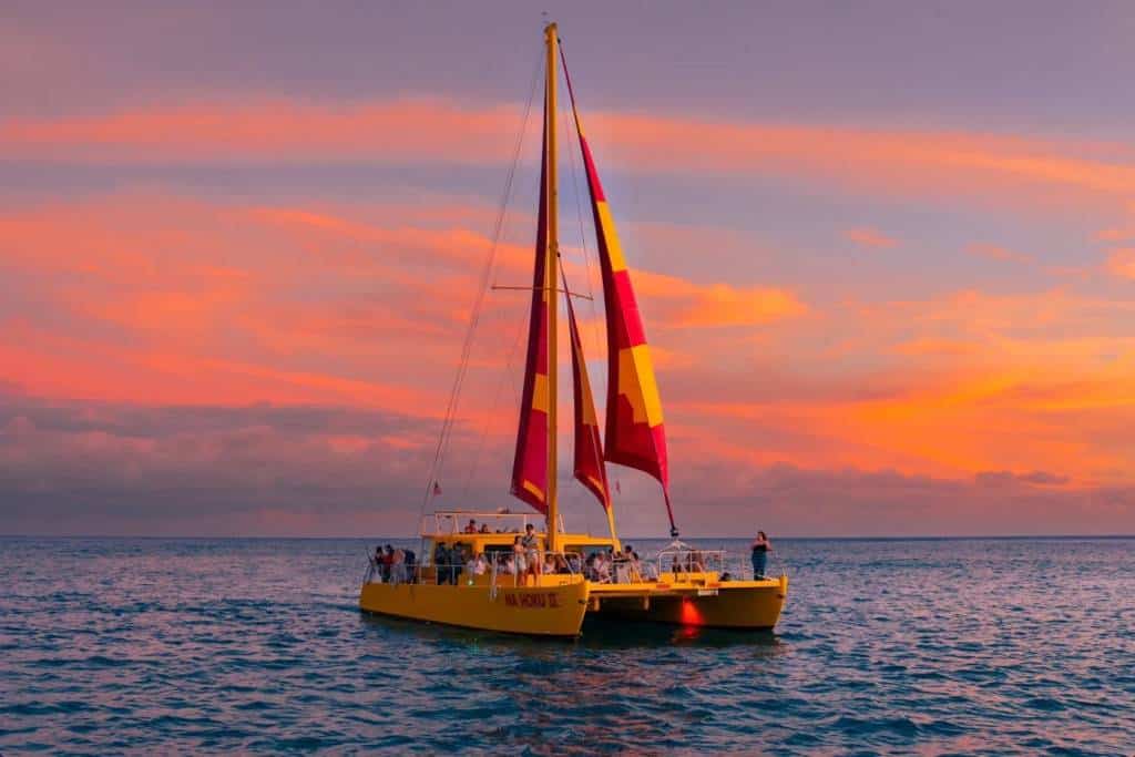 A catamaran under sail off Waikīkī at sunset